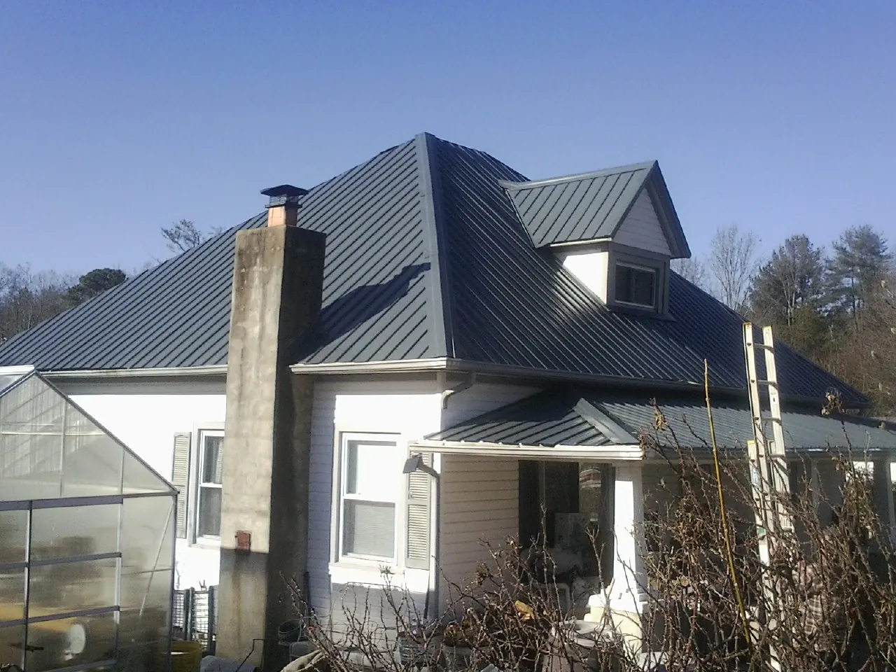 Dark blue standing seam metal roof on a white farmhouse with dormer — Slate & Tile Roof Repair by Roofing Brothers in Flatonia