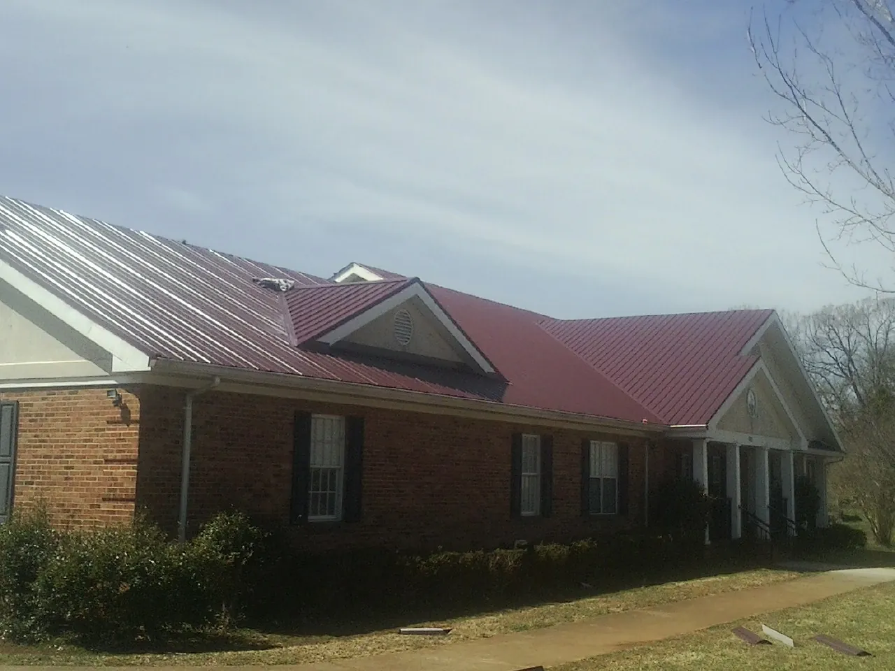 Red metal roof with gabled entries on a long brick building, from a Hail Damage Roof Repair job in Flatonia
