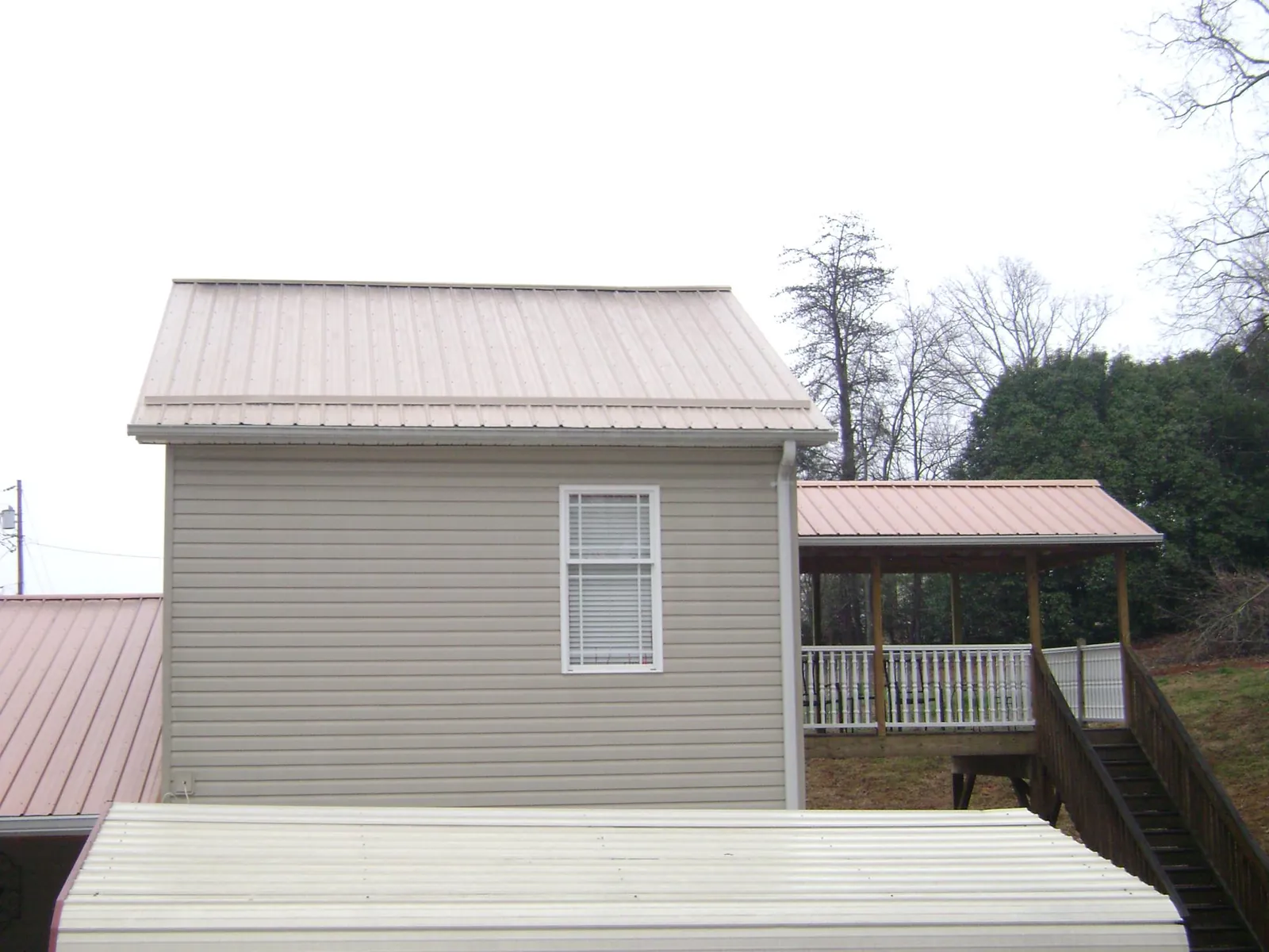Tan metal roofs on a two story addition and attached porch, from a Roof Replacement job in Flatonia